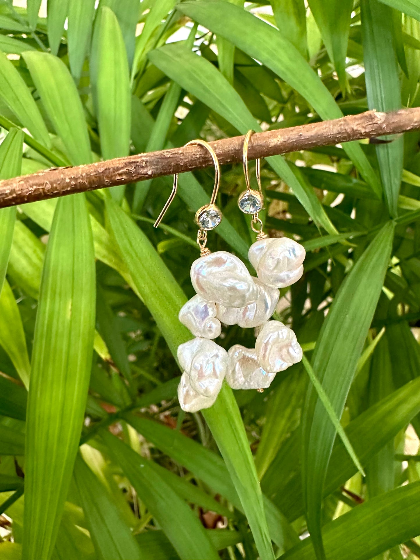 Pearl drop earrings featuring keshi pearls and blue CZ, handcrafted in Canada, hanging against lush green foliage.