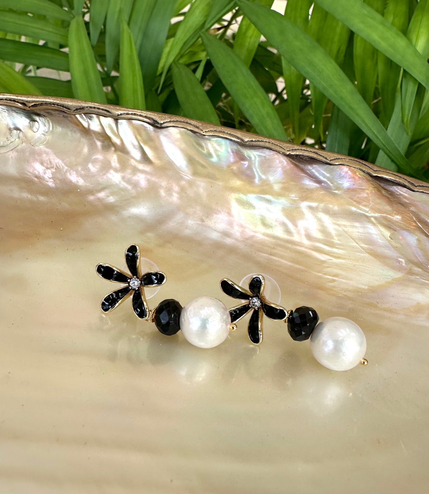 Edison pearl black spinel earrings styled on shell dish with greenery, black flower studs and white pearl drops