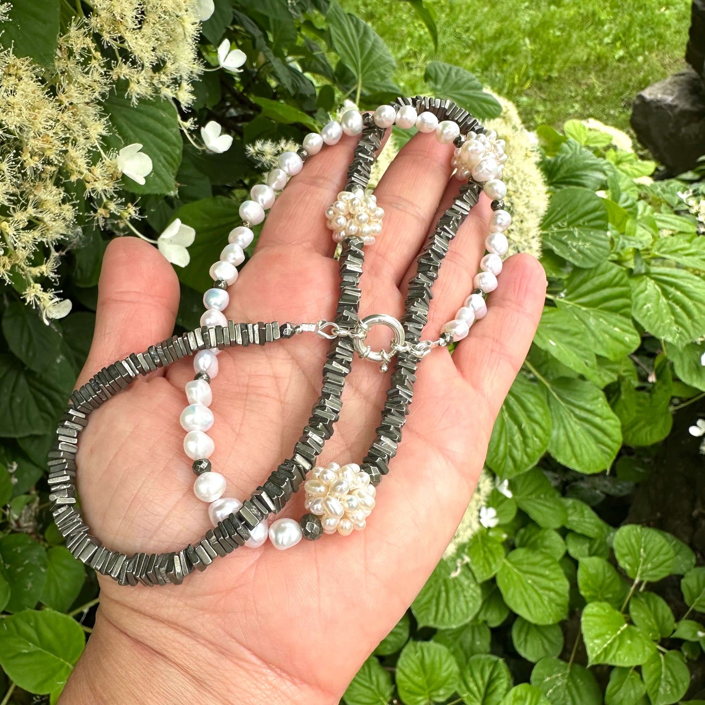 Pyrite and pearl necklace held in hand against green foliage