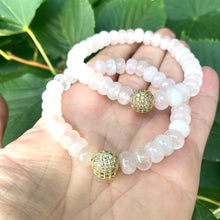 Load image into Gallery viewer, Rose quartz stretch bracelet with gold accent beads shown on a hand against green foliage.