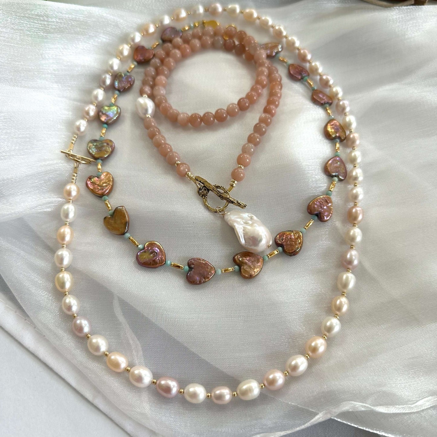 Sunstone necklace placed alongside two pearl necklaces on white cloth