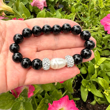 Load image into Gallery viewer, Black onyx bracelet with pearl held in hand against green foliage