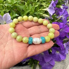 Load image into Gallery viewer, Olive green jade bracelet with one pearl held in hand near purple flowers