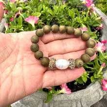 Load image into Gallery viewer, Hand holding gold druzy agate bracelet with pearl near a lakeside