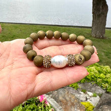 Load image into Gallery viewer, Gold druzy agate bracelet held in hand against green summer foliage