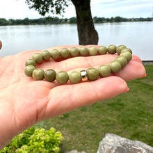 Load image into Gallery viewer, Olive Green Jasper Bracelet – 6mm or 8mm, 14K Gold Filled held in hand by a lakeside.