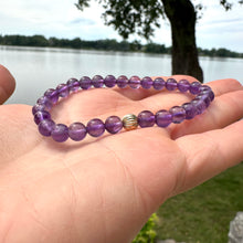 Charger l'image dans la galerie, Amethyst bracelet held in hand against lake and green foliage