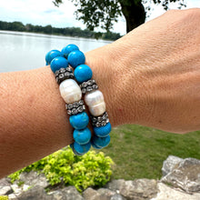 Load image into Gallery viewer, Turquoise howlite pearl bracelets worn on wrist beside garden lake