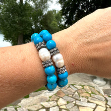 Load image into Gallery viewer, Two turquoise howlite pearl bracelets stacked on wrist near water in garden