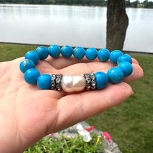 Load image into Gallery viewer, Turquoise howlite pearl bracelet held in hand against natural foliage