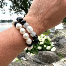 Load image into Gallery viewer, Two white pearl stretch bracelets with black rhinestones worn on woman's wrist in summer foliage