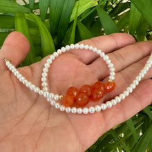 Load image into Gallery viewer, Double strand pearl bracelet held in hand against green foliage, showing natural light reflection