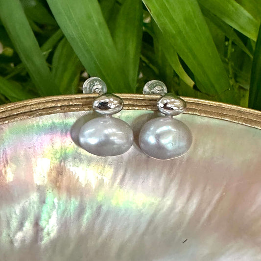 Silver grey nugget pearl stud earrings hanging from pearl shell with green leaf backdrop, handcrafted in Canada.