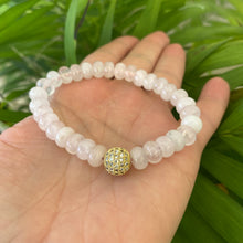 Load image into Gallery viewer, Rose quartz stretch bracelet with gold accent bead displayed on a hand surrounded by greenery.