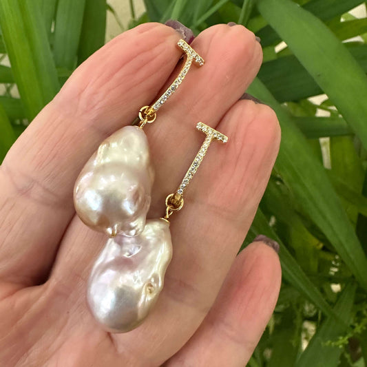 Pink baroque pearl hoop earrings held in hand against green foliage, designed and handmade in Canada.