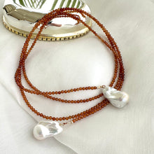 Load image into Gallery viewer, Hessonite Garnet and Baroque Pearl Lariat Necklace with gold-filled accents shown on white cloth background, designed and handmade in Canada.