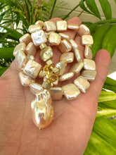 Charger l'image dans la galerie, Hand holding golden baroque pearl toggle necklace against leafy green background — lustrous baroque pearls and gold details by Loulia Pearl Jewelry