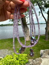 Charger l'image dans la galerie, Amethyst and Black Baroque Pearl Lariat Necklace held outdoors against lake and grass background — natural gemstone jewelry by Loulia Pearl Jewelry