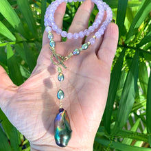Charger l'image dans la galerie, Amethyst Pearl Necklace with lavender beads and black baroque pearl held in hand against green foliage background.