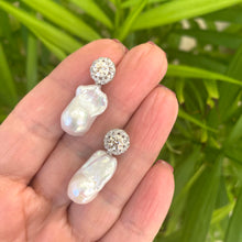 Charger l'image dans la galerie, Moissanite and baroque pearl earrings held in hand against green leaves, handmade jewelry display.