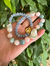 Charger l'image dans la galerie, Blue jade morganite aquamarine pearl necklace showcasing baroque gem design, held in hand among lush foliage.