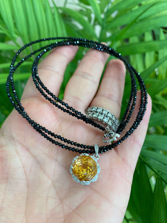 Hand holding black spinel and citrine pendant necklace near green leaf background