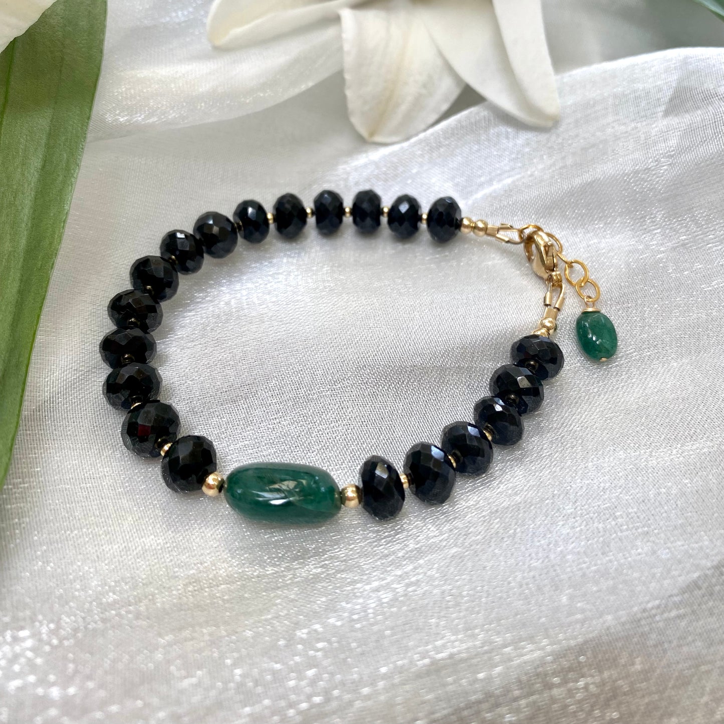 Spinel emerald bracelet featuring black spinel beads and a green emerald centerpiece on a silky background.