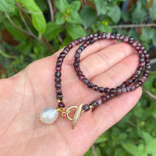 Load image into Gallery viewer, Garnet toggle necklace with baroque pearl charm elegantly displayed in a hand, featuring faceted garnet cube beads.