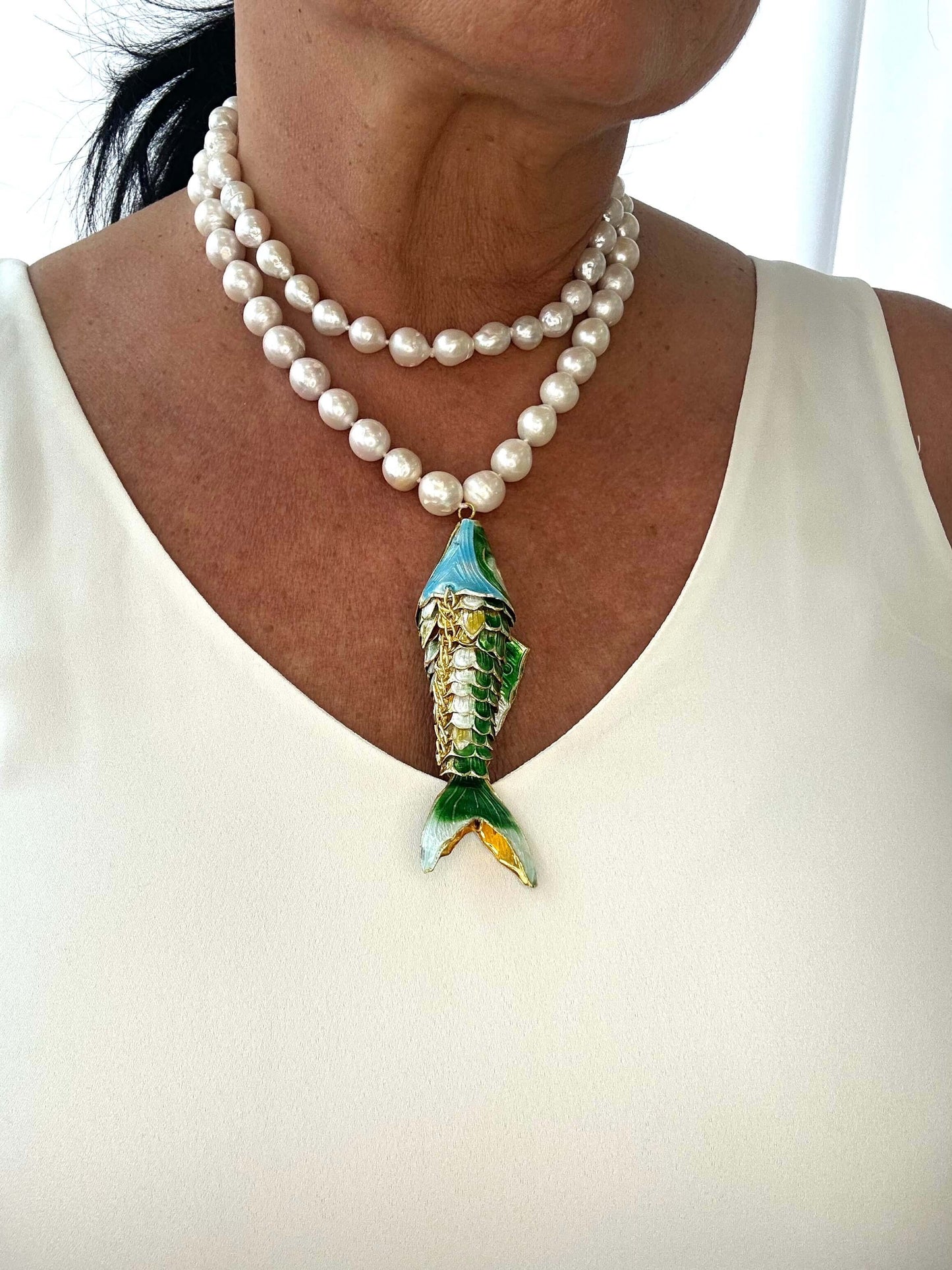 Pearl necklace with a fish-shaped pendant worn by a person on a white background