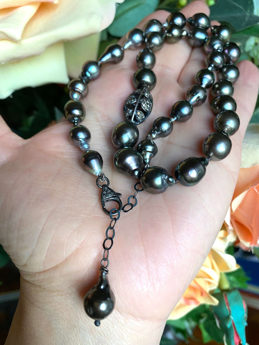 Tahitian baroque pearl necklace with champagne diamonds displayed in hand among blooming roses.