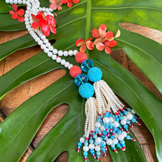 Pearl coral turquoise lariat necklace featuring freshwater pearls, coral, and turquoise beads on a tropical leaf backdrop.