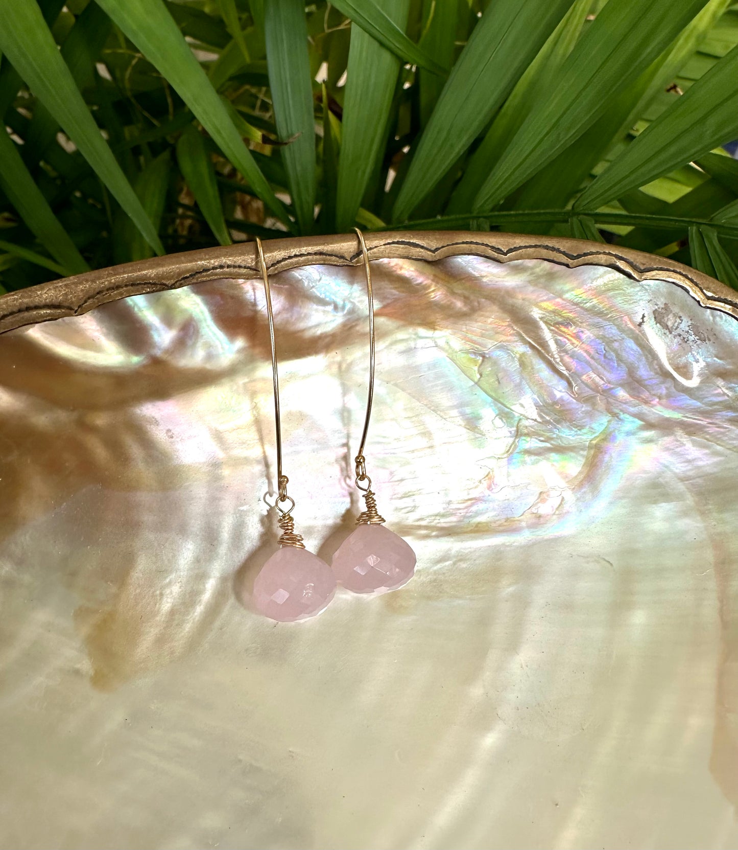 Rose quartz threader earrings with briolettes displayed on a pearl shell, showcasing their delicate design and soft pink hues.