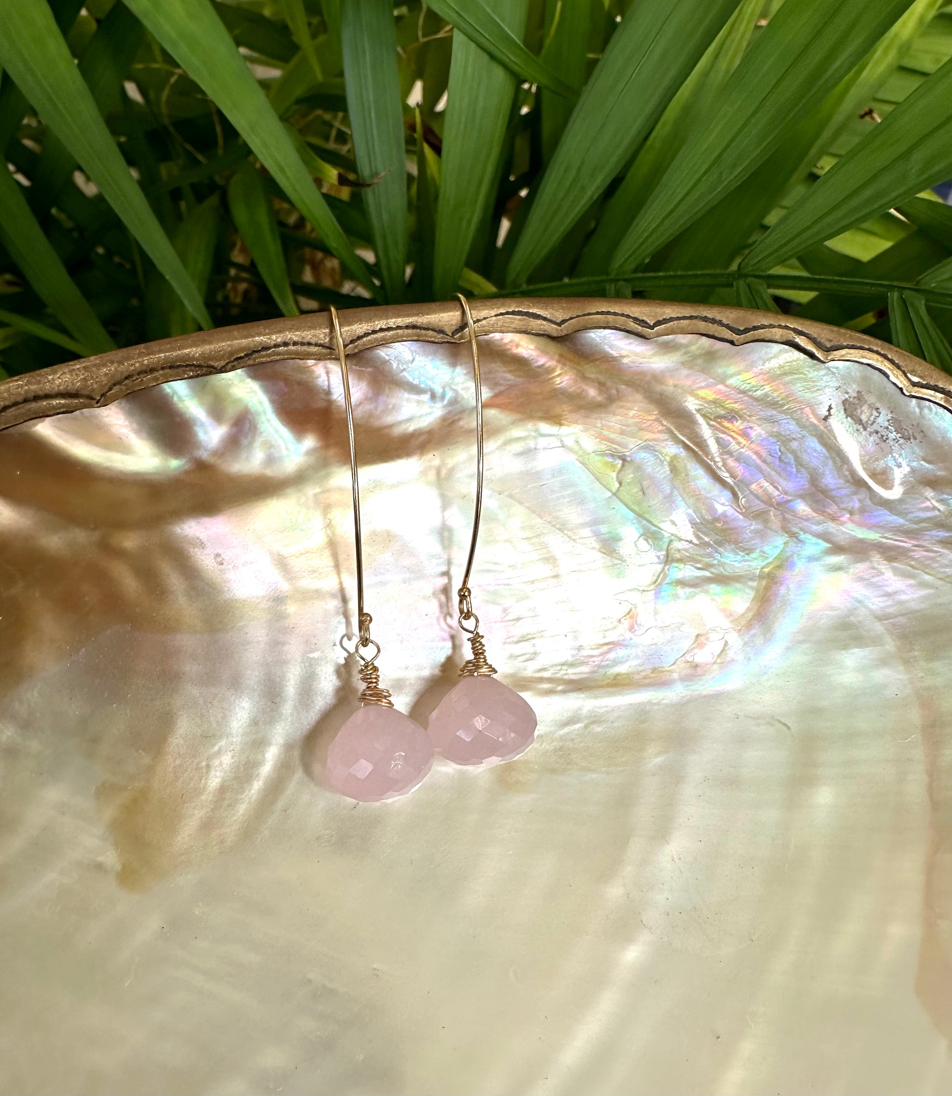 Rose quartz threader earrings with briolettes displayed on a pearl shell, showcasing their delicate design and soft pink hues.