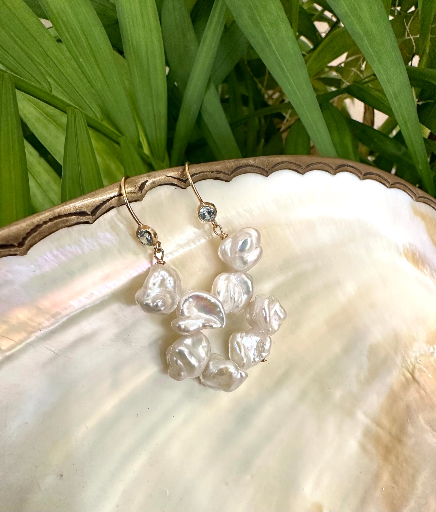 Pearl drop earrings featuring keshi pearls and blue CZ, elegantly displayed on a seashell with greenery.