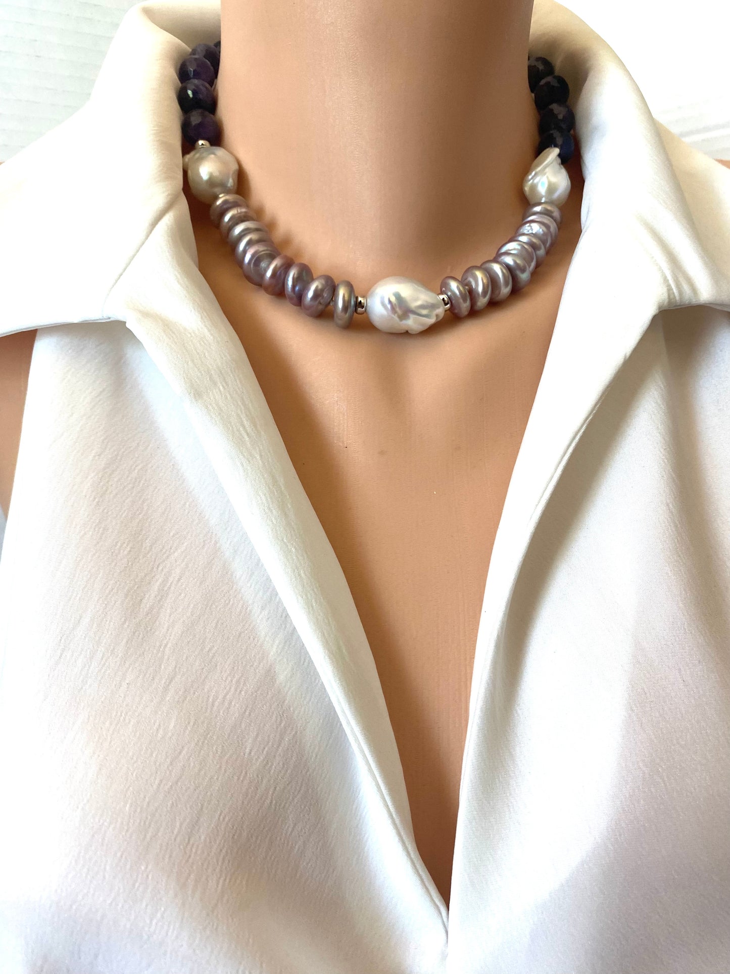 A close-up of a double-strand pearl necklace worn on a mannequin torso wearing a white satin shirt. The necklace features a top strand of dark purple beads and a bottom strand of silver-gray and white baroque pearls.