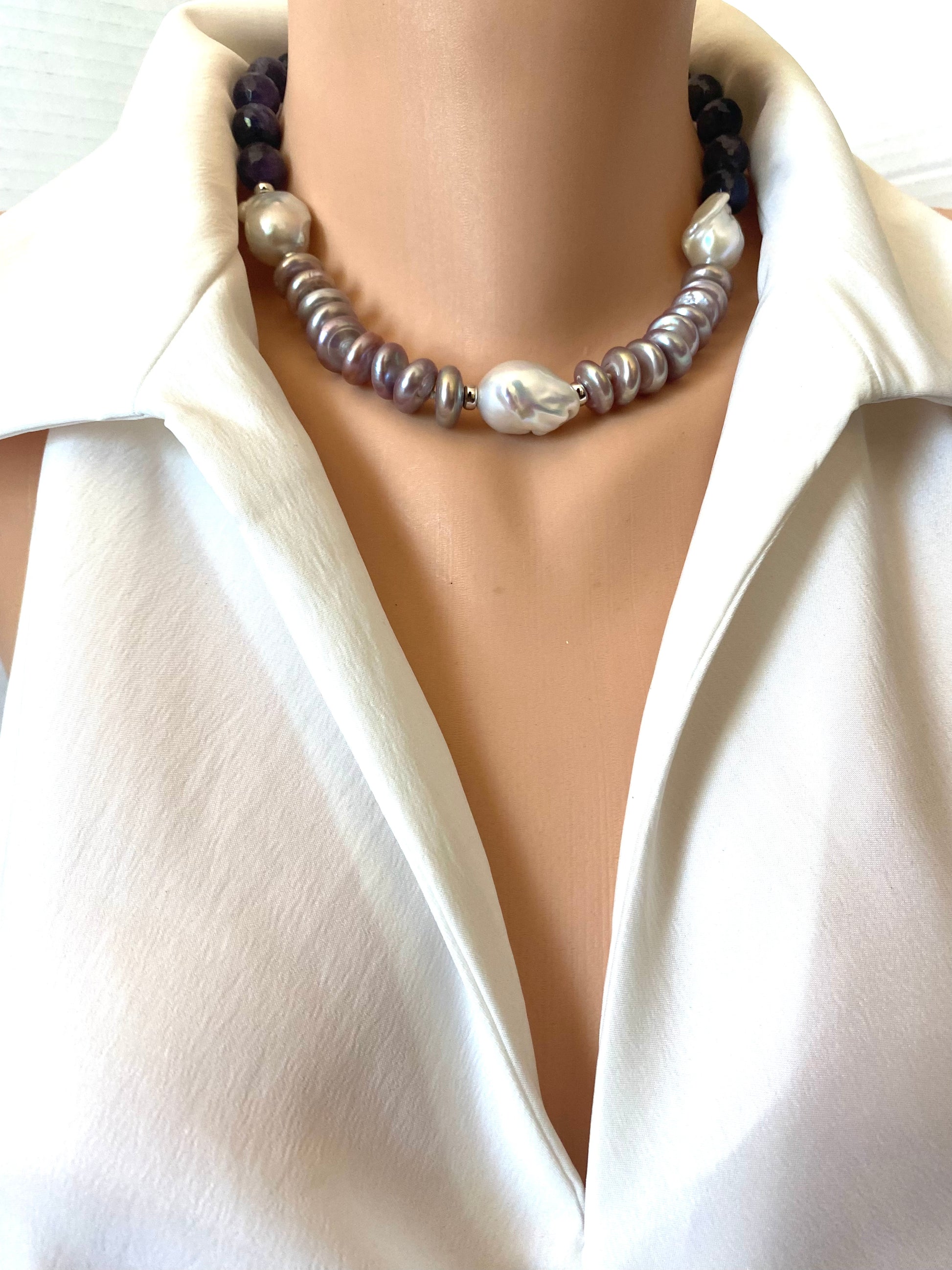 A close-up of a double-strand pearl necklace worn on a mannequin torso wearing a white satin shirt. The necklace features a top strand of dark purple beads and a bottom strand of silver-gray and white baroque pearls.