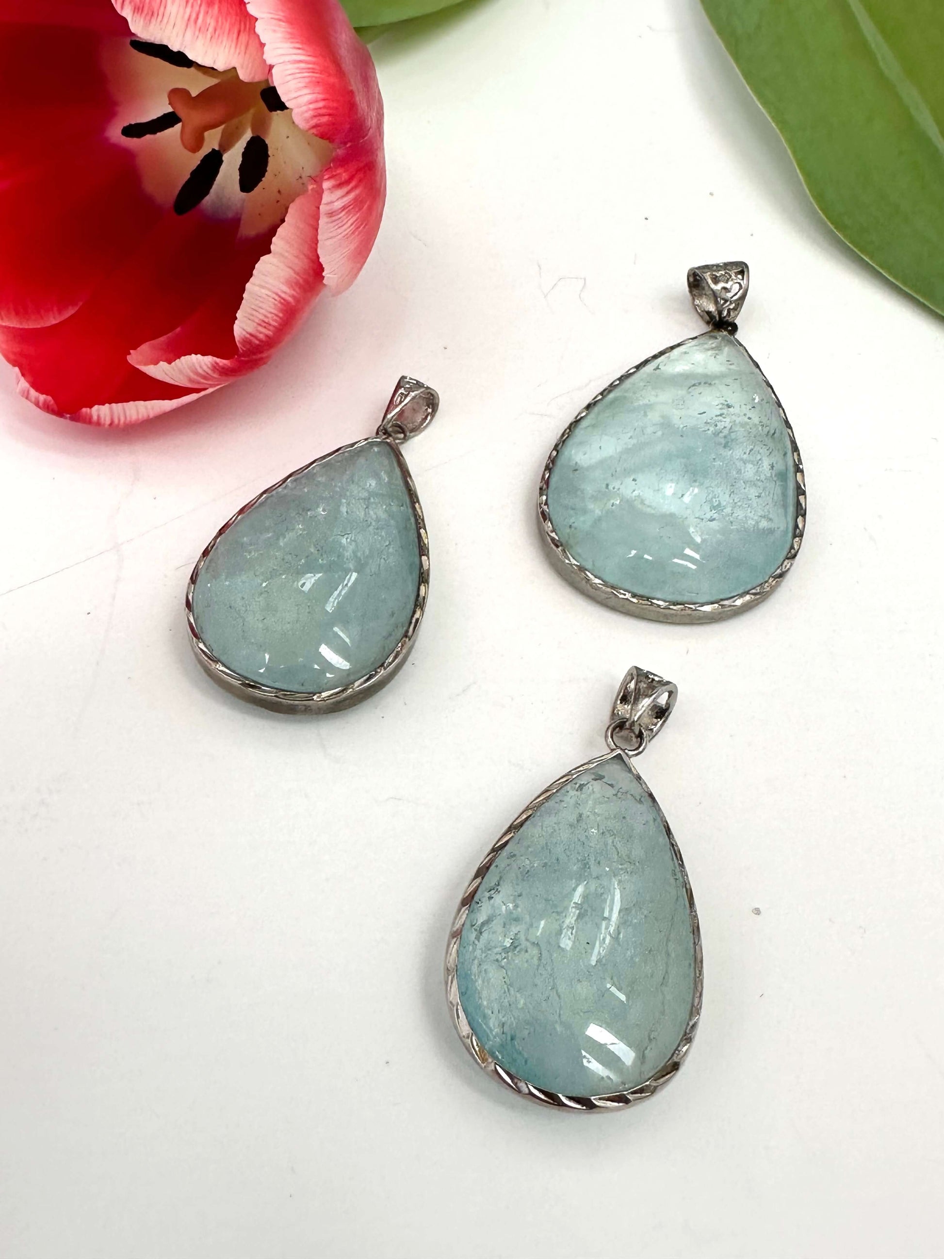 Aquamarine teardrop pendant in oxidized sterling silver, showcasing pear-shaped stones against a floral background.