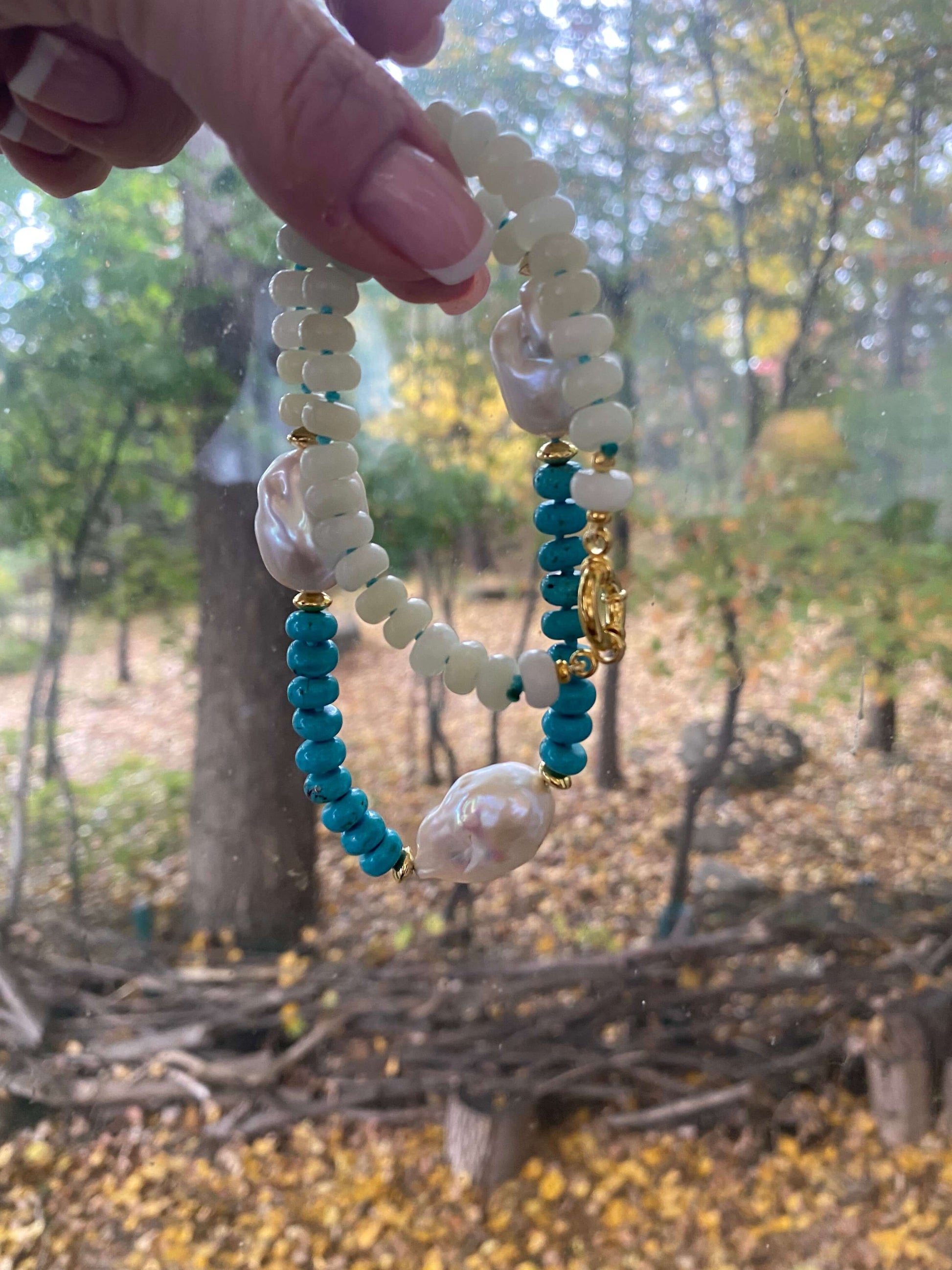 Detail view of handmade green jade and turquoise pearl necklace near leaves