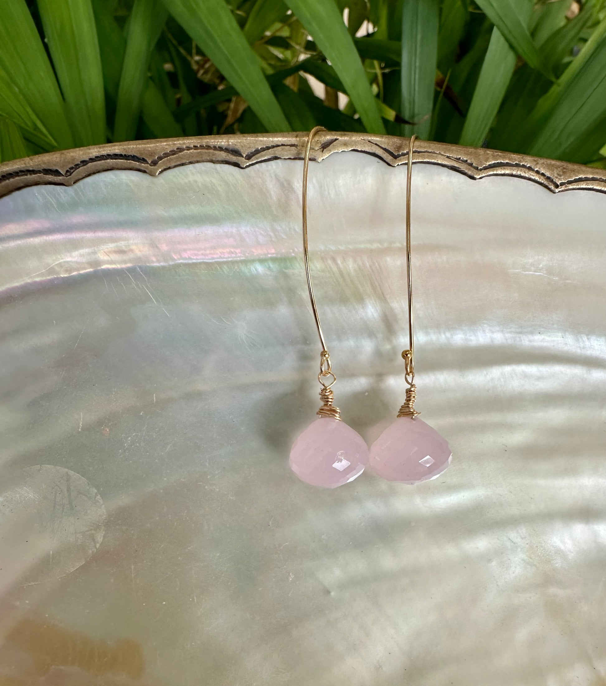 Rose quartz threader earrings with briolettes displayed on a silver plate surrounded by greenery.