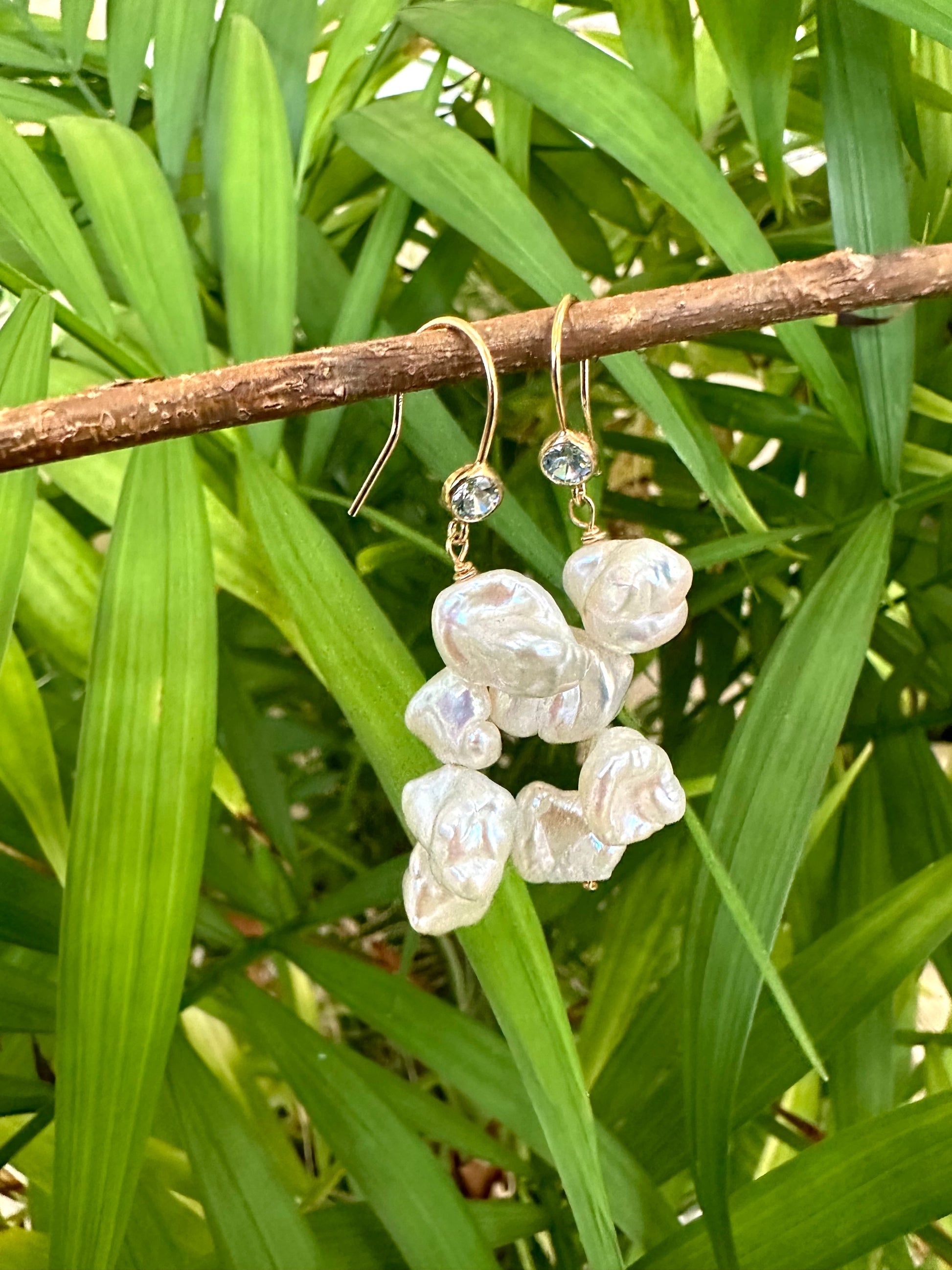 Pearl drop earrings featuring keshi pearls and blue CZ, handcrafted in Canada, hanging against lush green foliage.