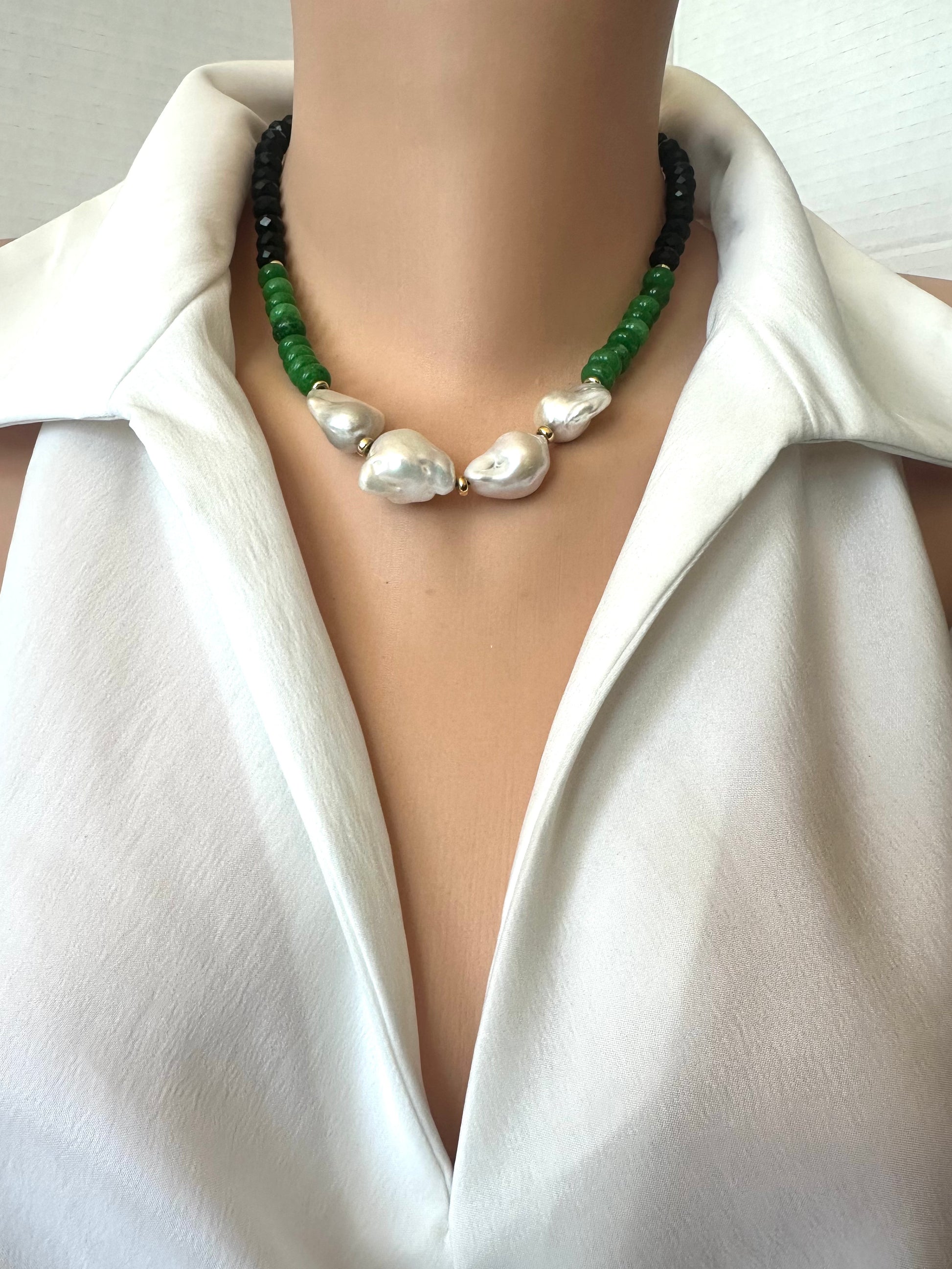 A close-up of a necklace worn on a mannequin or model torso, featuring 4 large irregular white baroque pearls in the center, flanked by green beads and black beads, styled with a white collared shirt.