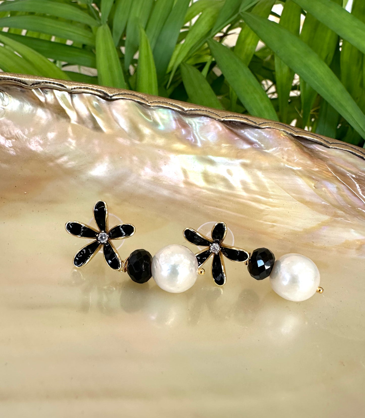 Edison pearl black spinel earrings flat lay on shell dish with greenery, black enamel flower studs and white pearls