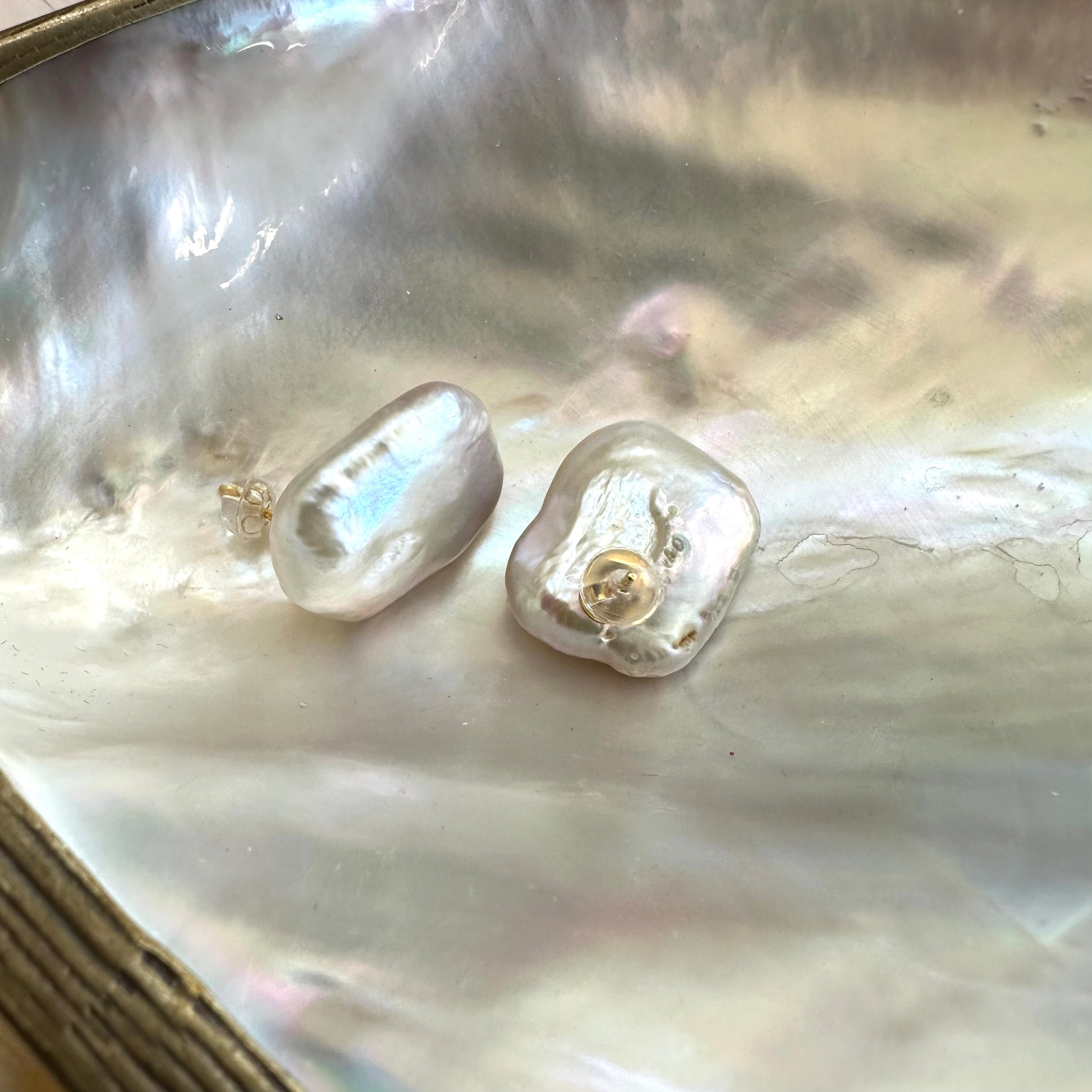 Baroque pearl stud earrings with oversized white rectangular pearls resting on shell, showing soft sheen and natural texture.
