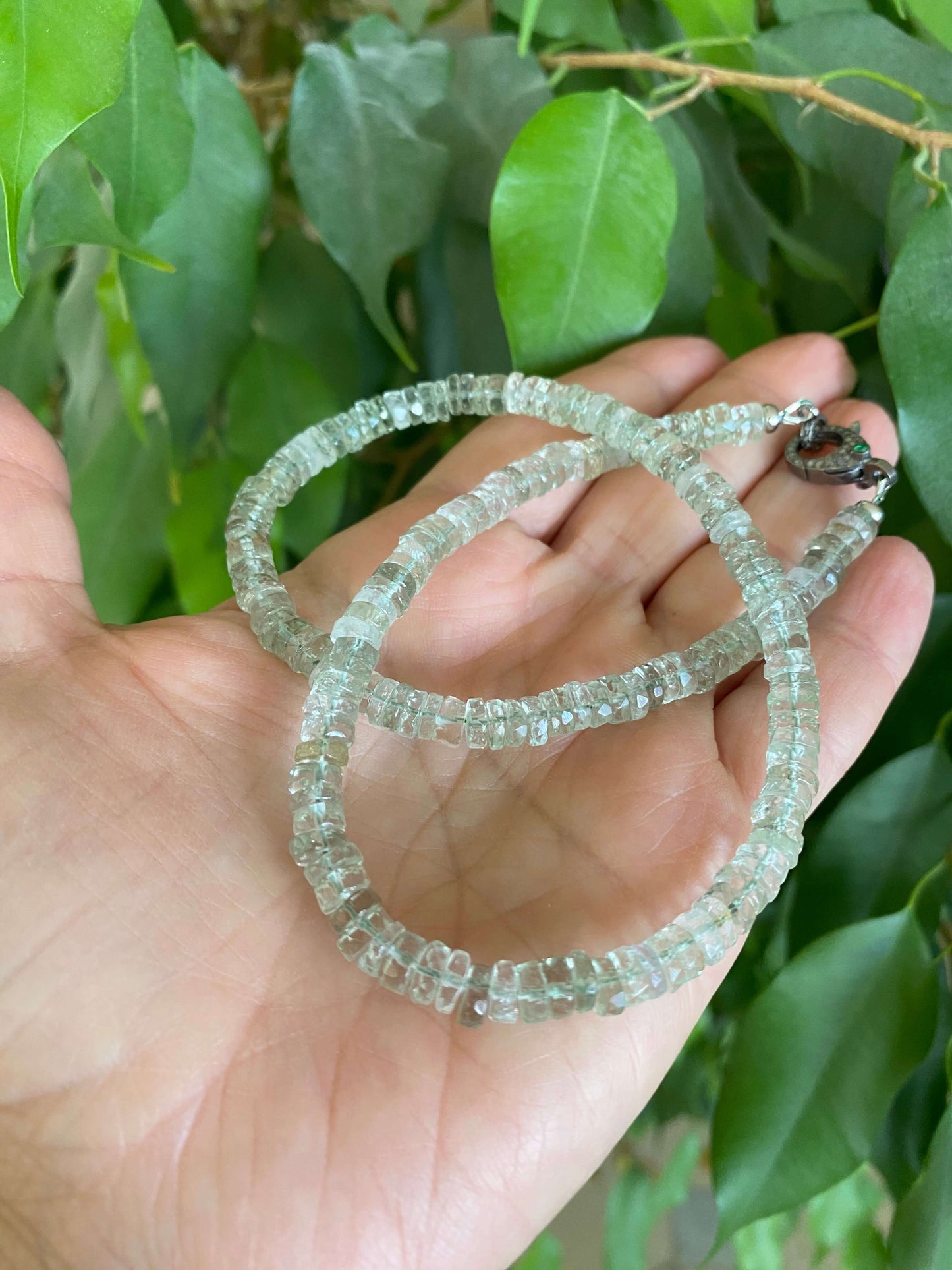 Green amethyst beaded necklace with diamond & emerald pavé clasp held in hand against green foliage.