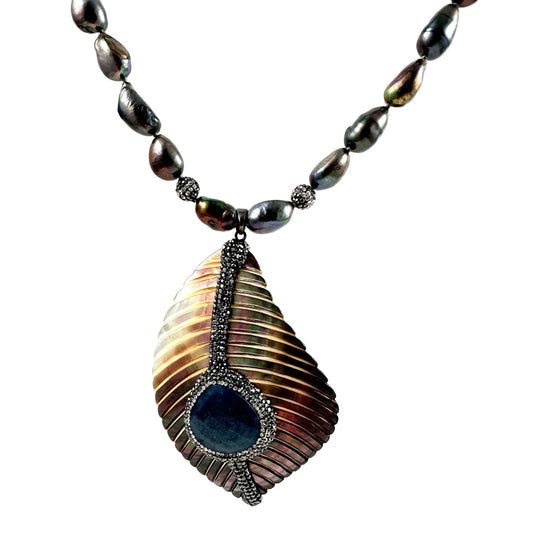 A dark, iridescent baroque pearls and a large, textured teardrop-shaped pendant with a dark blue center stone and silver-toned metal detailing, set against a plain white background.