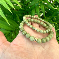 Olive green jasper bracelet showcasing 6mm and 8mm beads in a hand, featuring gold accents and lush green background.
