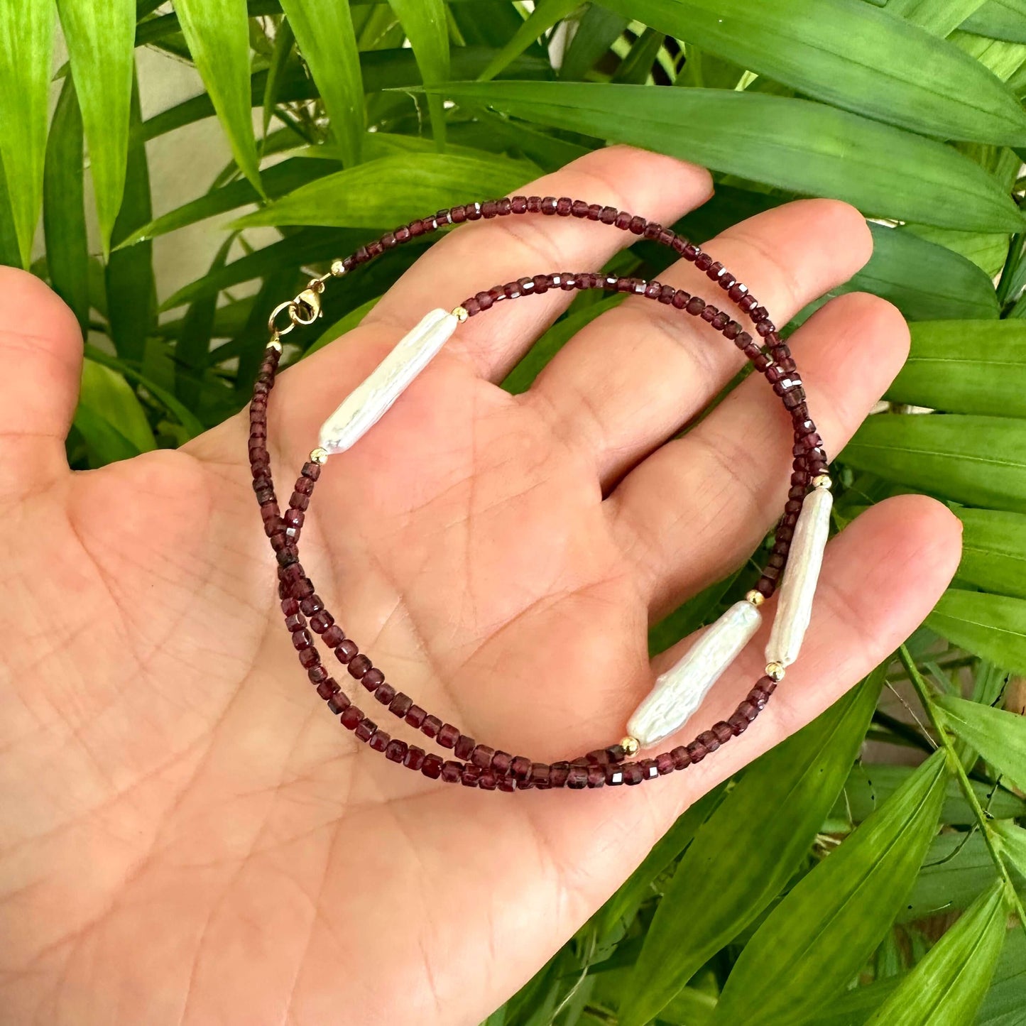 Garnet Pearl Necklace with Baroque pearls held in hand against foliage – detailed shot