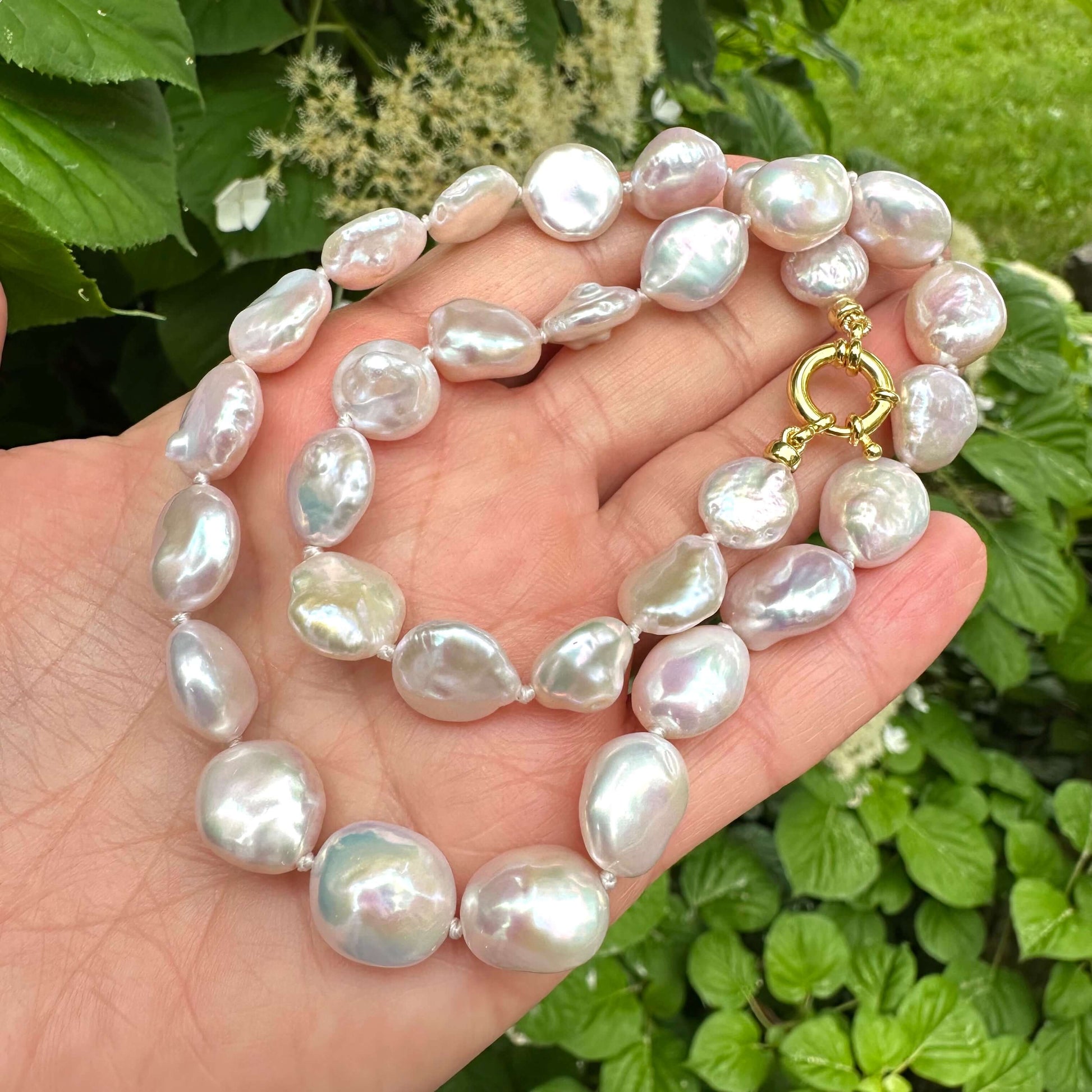 Close-up of coin pearl necklace held in hand against summer foliage