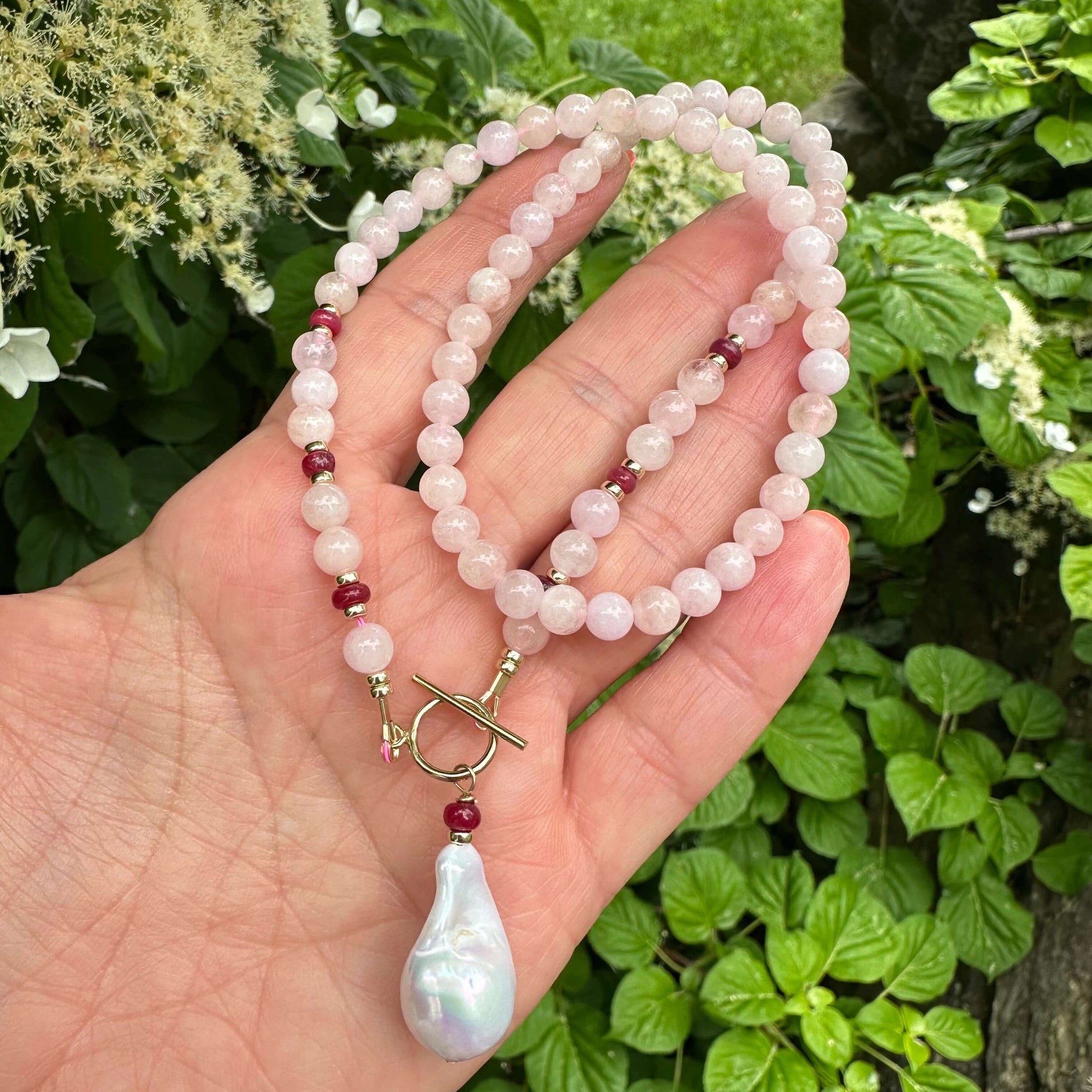 Morganite necklace with ruby rondelles held in hand near green foliage