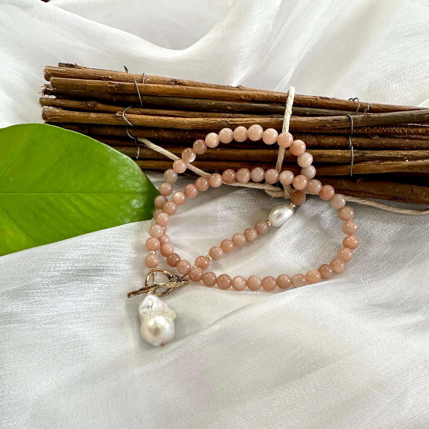 Sunstone necklace with gold bronze toggle and baroque pearl displayed on white cloth